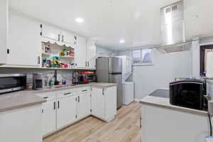 Kitchen with island exhaust hood, appliances with stainless steel finishes, white cabinetry, and open shelves