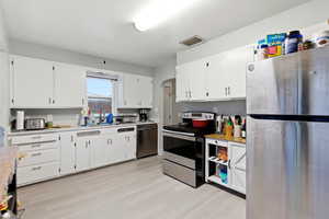Kitchen featuring stainless steel appliances, arched walkways, white cabinetry, and light wood-style floors