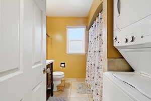 Bathroom with light tile patterned floors, stacked washing machine and dryer, curtained shower, and vanity