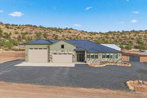 View of front of property featuring stone siding, driveway, a metal roof, and an attached garage