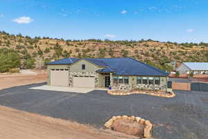 View of front of house featuring stone siding, gravel driveway, a garage, and a metal roof