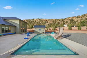 View of swimming pool with a water slide, a patio area, a fenced backyard, and an outdoor structure