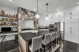 Kitchen featuring stainless steel appliances, hanging light fixtures, a kitchen breakfast bar, white cabinets, and a center island