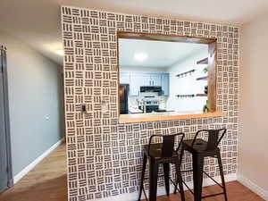 Bar area with freestanding refrigerator, wood finished floors, stainless steel electric range oven, light countertops, and under cabinet range hood