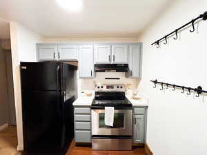 Kitchen featuring gray cabinets, electric stove, light countertops, freestanding refrigerator, and under cabinet range hood