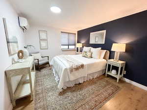 Bedroom with crown molding, wood finished floors, and a wall unit AC