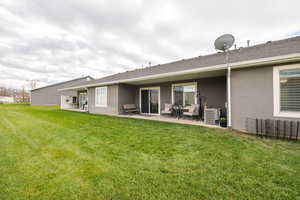 Rear view of house featuring stucco siding, a patio area, a yard, and roof with shingles