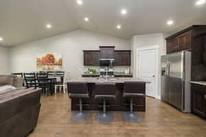 Kitchen featuring dark brown cabinetry, open floor plan, appliances with stainless steel finishes, light stone counters, and recessed lighting
