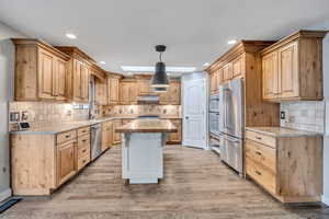 Kitchen featuring pendant lighting, a kitchen bar, stainless steel appliances, light wood-type flooring, and light brown cabinets