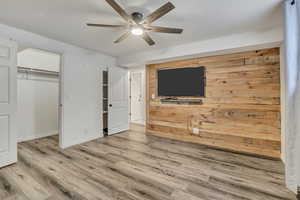 Unfurnished bedroom featuring wooden walls, wood finished floors, ceiling fan, a walk in closet, and an accent wall