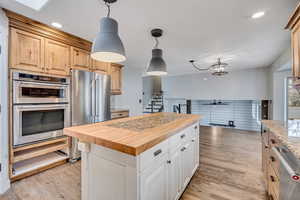 Kitchen with butcher block countertops, hanging light fixtures, stainless steel appliances, light wood finished floors, and recessed lighting
