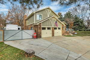 View of home's exterior with board and batten siding, brick siding, driveway, a gate, and a chimney