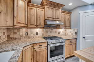 Kitchen with gas stove, under cabinet range hood, tasteful backsplash, and light stone counters