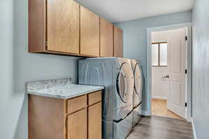 Laundry room featuring wood finished floors, washer and clothes dryer, and cabinet space