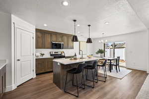 Kitchen featuring recessed lighting, pendant lighting, a kitchen island with sink, a textured ceiling, and a breakfast bar area
