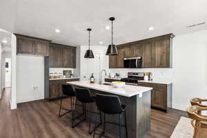 Kitchen featuring dark brown cabinets, a kitchen breakfast bar, recessed lighting, appliances with stainless steel finishes, and a kitchen island with sink