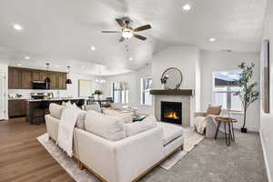 Living room featuring lofted ceiling, a ceiling fan, a fireplace, a chandelier, and recessed lighting