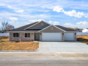 View of front facade featuring an attached garage, driveway, board and batten siding, stone siding, and roof with shingles