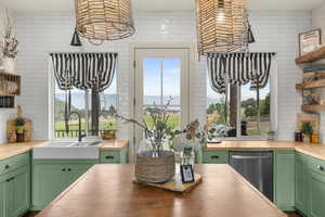 Kitchen with green cabinets, open shelves, wooden counters, tasteful backsplash, and stainless steel dishwasher