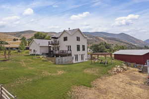 Back of house featuring a lawn, a deck with mountain view, and a balcony