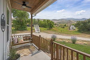Covered porch with a mountain view, ceiling fan, and a lawn