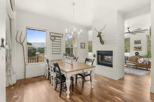 Dining room with a multi sided fireplace, light wood-style flooring, a chandelier, and a ceiling fan