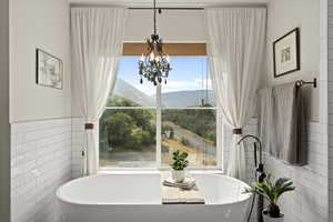Full bath with a soaking tub, tile walls, a chandelier, wainscoting, and a mountain view