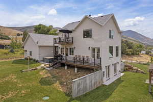 Rear view of property with a lawn, roof with shingles, a deck with mountain view, a balcony, and a patio