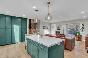 Kitchen with tloans of storage floor to ceiling teal cabinetry, a center island, light LVP flooring, recessed lighting, and a breakfast bar area