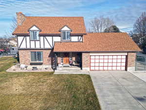Tudor-style house with a chimney, roof with shingles, a front lawn, driveway, and a garage