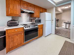 Kitchen featuring light countertops, brown cabinets, range with electric stovetop, and decorative backsplash