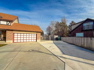 View of side of home with brick siding, driveway, roof with shingles, and a gate