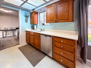Kitchen featuring brown cabinetry, light countertops, stainless steel dishwasher, a wainscoted wall, and light floors