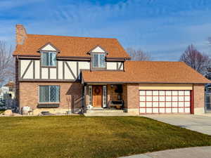Tudor-style house with roof with shingles, a front lawn, covered porch, concrete driveway, and an attached garage