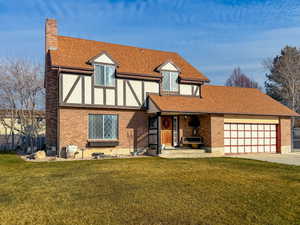 English style home featuring a shingled roof, a front yard, a chimney, and brick siding