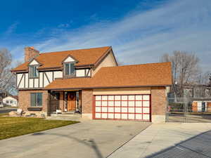 Tudor home featuring a shingled roof, driveway, a chimney, and brick siding