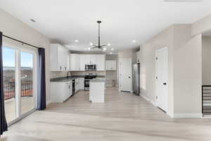 Kitchen with a chandelier, stainless steel appliances, a kitchen island, decorative light fixtures, and white cabinetry