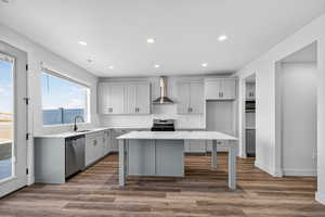 Kitchen featuring gray cabinets, a kitchen island, wall chimney exhaust hood, stainless steel appliances, and light stone countertops