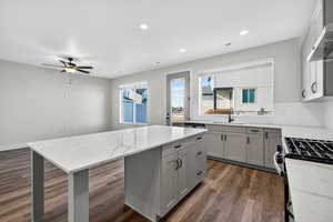 Kitchen with light stone counters, dark wood finished floors, gray cabinetry, a center island, and decorative backsplash