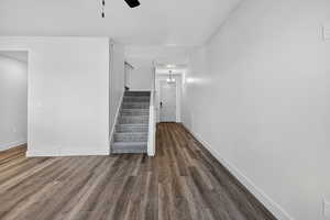 Unfurnished living room with stairway, ceiling fan, dark wood-style flooring, and a chandelier