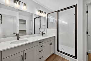 Full bathroom featuring a spacious closet, double vanity, a marble finish shower, and light wood-type flooring