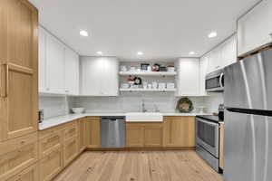 Kitchen with open shelves, stainless steel appliances, light wood flooring, recessed lighting.