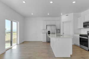 Kitchen with appliances with stainless steel finishes, light wood-style flooring, white cabinets, a kitchen island with sink, and recessed lighting