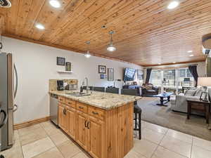 Kitchen featuring a peninsula, wood ceiling, decorative light fixtures, light stone counters, and a breakfast bar