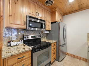 Kitchen featuring stainless steel appliances, wood ceiling, light stone countertops, crown molding, and decorative backsplash