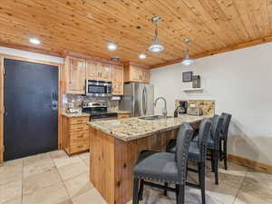 Kitchen with light stone counters, wood ceiling, hanging light fixtures, a peninsula, and a kitchen breakfast bar