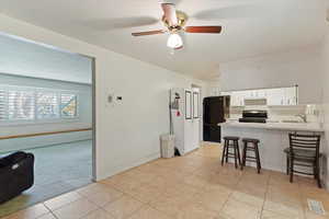 Kitchen with a kitchen breakfast bar, light countertops, black appliances, a ceiling fan, and white cabinets
