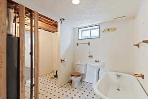 Full bathroom featuring a freestanding tub, a textured ceiling, and water heater