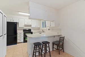 Kitchen featuring black appliances, light countertops, a breakfast bar, a peninsula, and light tile patterned floors