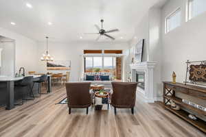 Living room featuring a ceiling fan, recessed lighting, light wood-style flooring, a glass covered fireplace, and a chandelier
